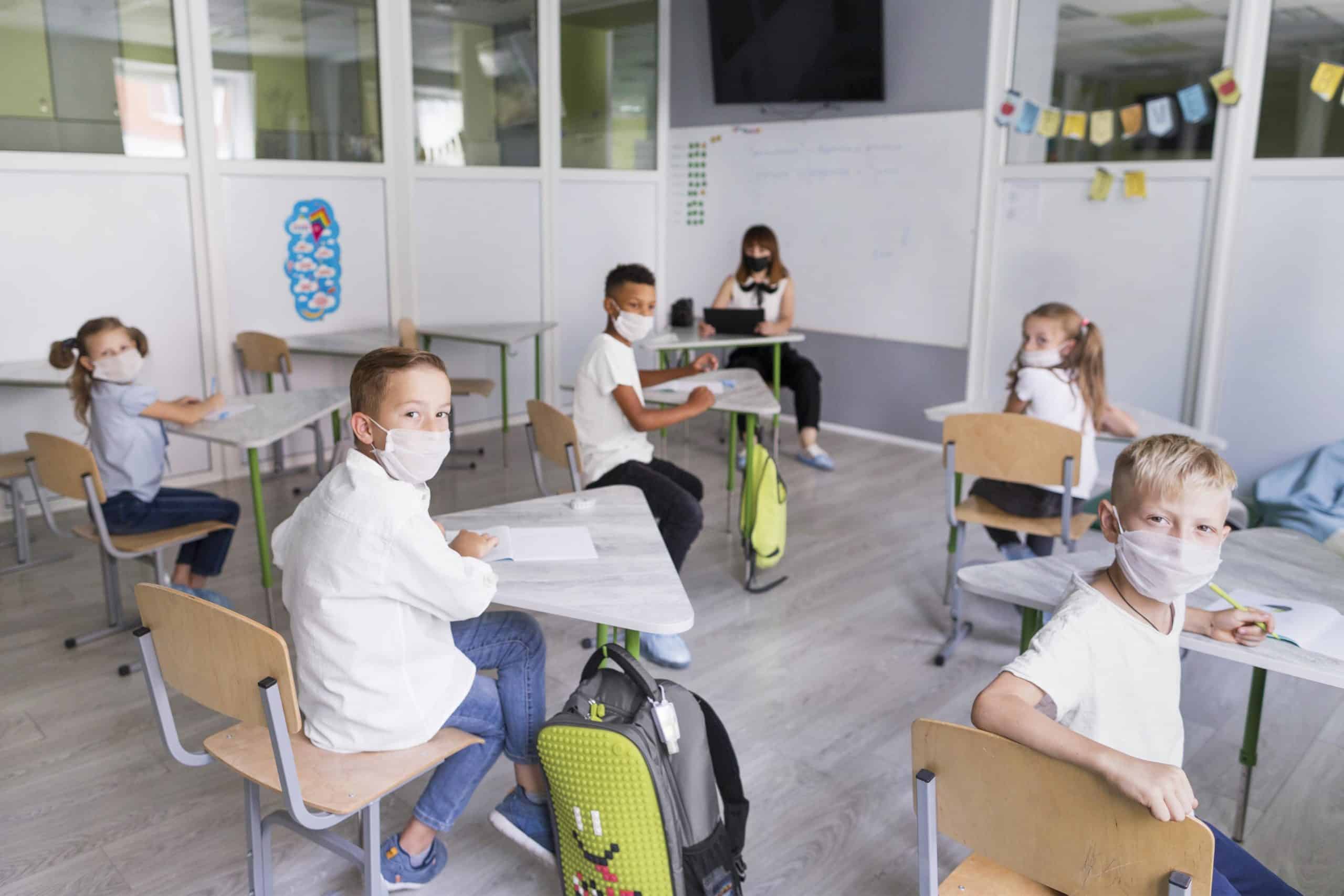 Students sitting in class room wearing safety face masks and social distancing