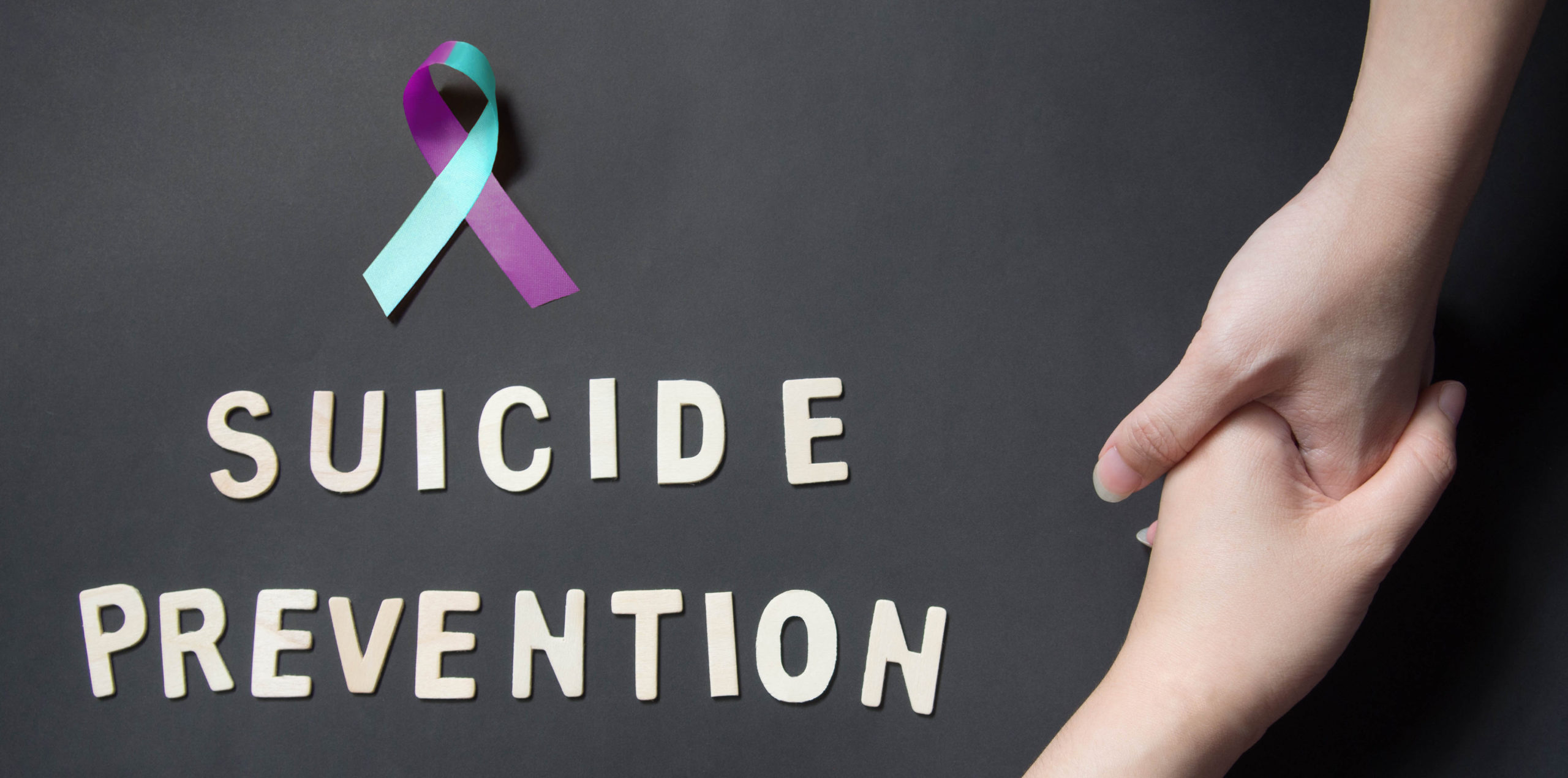 Purple and teal suicide awareness ribbon and people holding hands, with the words suicide prevention to the left